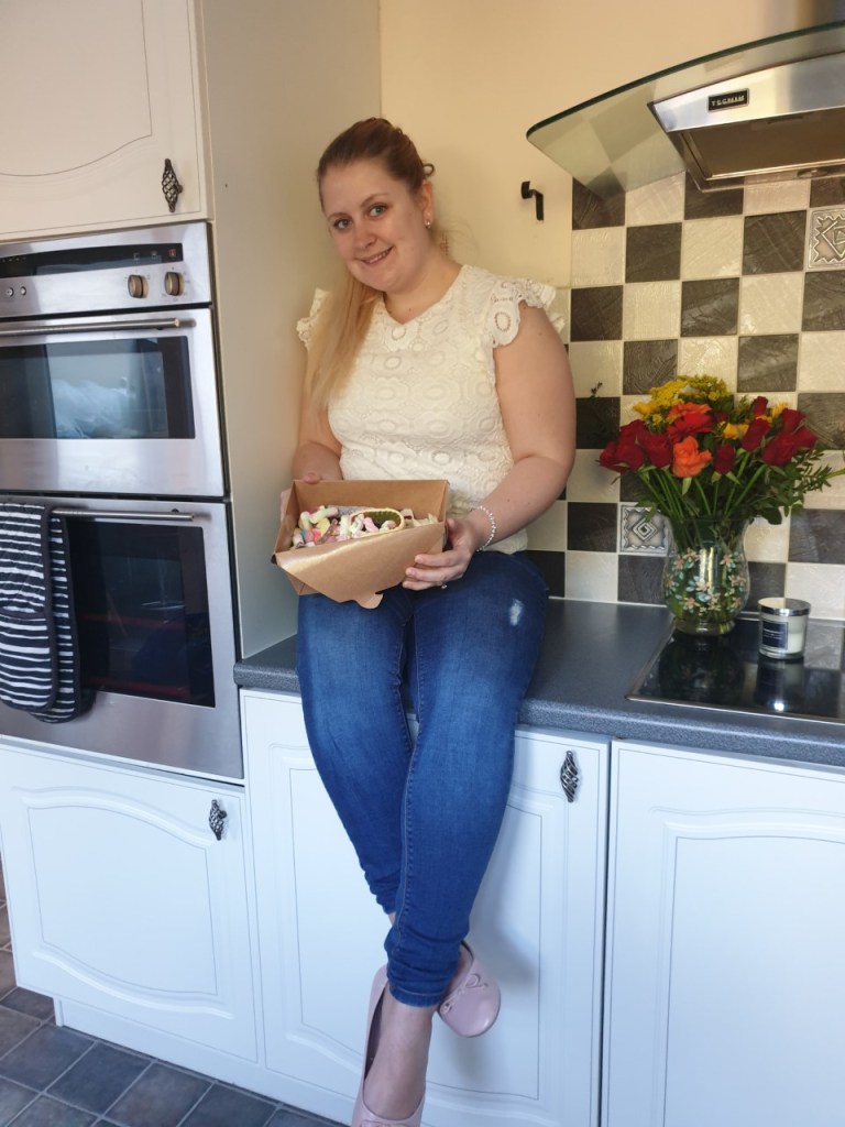 Blonde female sat on kitchen worktop with a box of Panda Sweets Pick N Mix