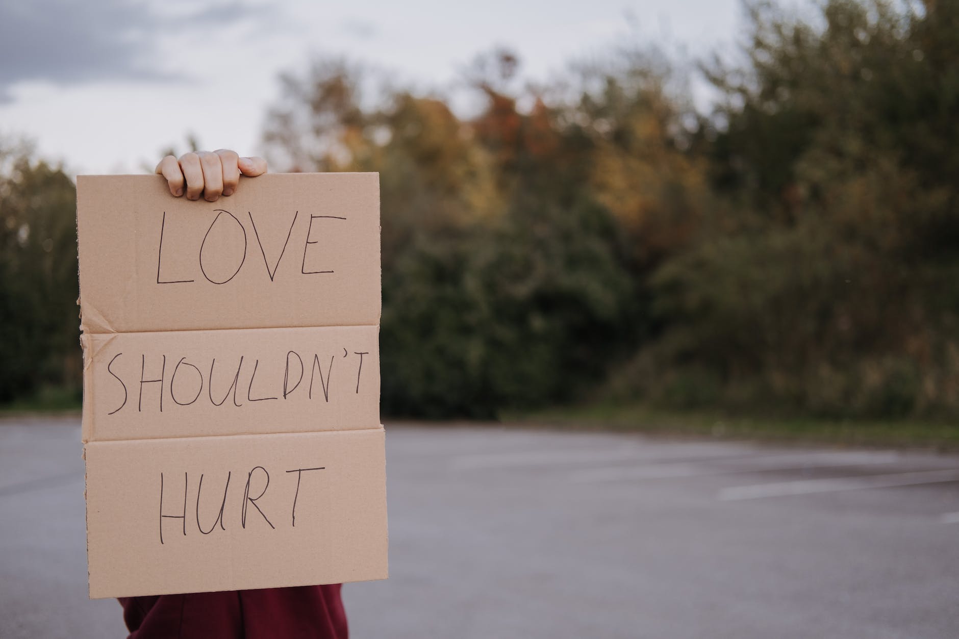 person with carton with inscription love should not hurt for how to spot the signs of an abusive relationship post.
