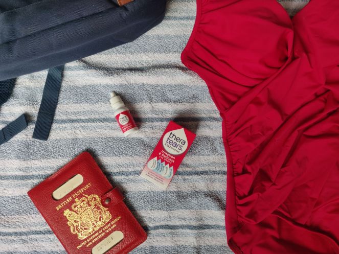 Flatlay of swimsuit, passport and TheraTears Box and bottle for spring allergy eye relief: how to reduce redness, itchiness, and dryness post.