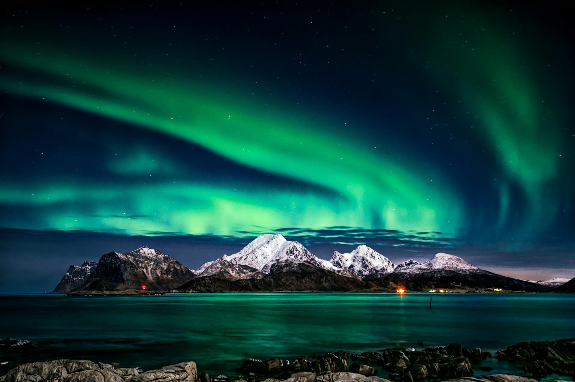 View of the northern lights over a lake with mountains in the background for Top Winter Travel Destinations You Must Book Now post.