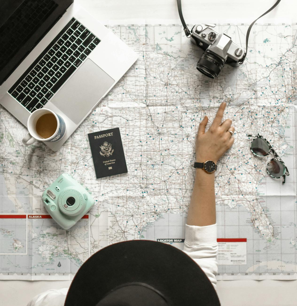 Flatlay of a map with a camera, passport, laptop, cup and sunglasses on top for 2025 Summer Travel Trends Everyone Is Talking About post.