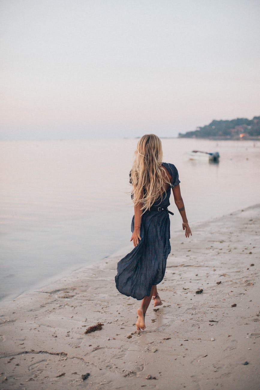 woman walking along the beach with her back to the camera for Summer Reset Checklist: How to Reboot Your Routine Mid-Year (Without Burning Out) post.